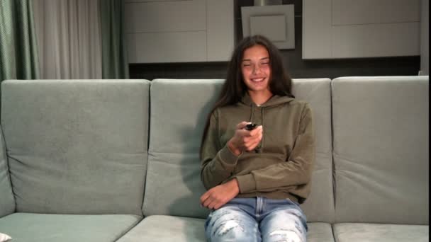 Mooie jonge dame in hoodie en jeans horloges televisie — Stockvideo