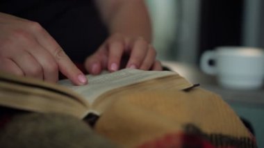 kadın odada kahverengi battaniye altında eski kitap sayfaları çevirir