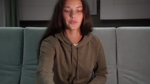 Pretty teenager in hoodie switches on television and eats — Stock Video