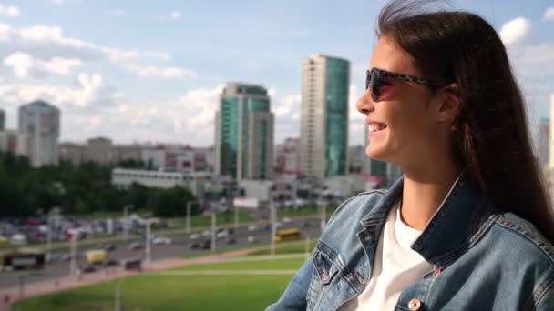 Красива брюнетка в чорних сонцезахисних окулярах дивиться на міський пейзаж — стокове відео