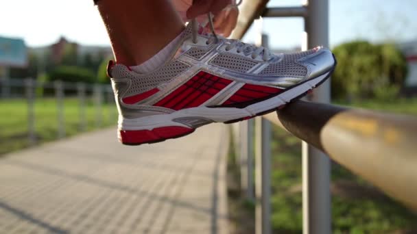 スポーティな女性は、金属手すりに足を置くレースを結び、実行します — ストック動画