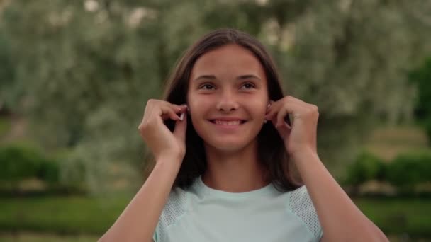 Menina sorridente em t-shirt branca coloca em fones de ouvido câmera lenta — Vídeo de Stock