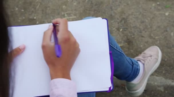 Молодая женщина открывает тетрадь и начинает писать письмо — стоковое видео