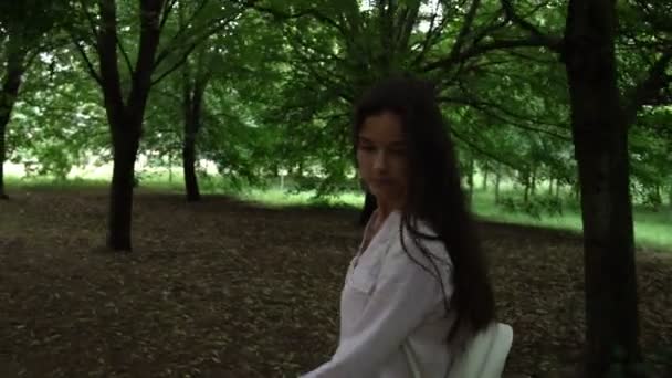 Jovem mulher bonita vagueia entre árvores no caminho do parque verde — Vídeo de Stock