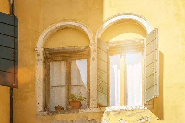 bright sunlight reflected in windows with open shutters in old house with yellow ragged wall