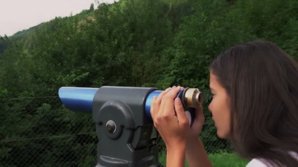 Flicka tittar på berg med skog i turistiska teleskop — Stockvideo