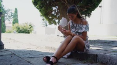 kız taş kaldırım üzerinde oturur ve akıllı telefonda internette sörf