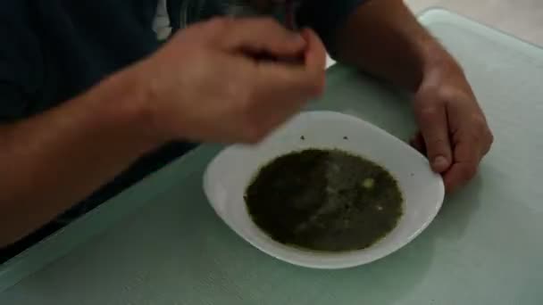 Kapüşonlu adam yeşil kuş çorbası içerek yemek yer. — Stok video