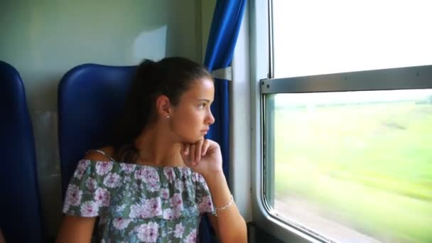 Young girl props head and looks outside train window — Stock Video