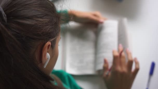 Старшокласниця в бездротових навушниках пише домашнє завдання — стокове відео
