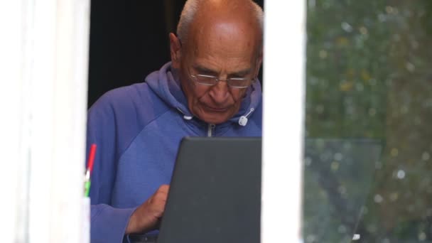 Senior hombre trabaja en gris portátil en el alféizar de la ventana de cámara lenta — Vídeos de Stock