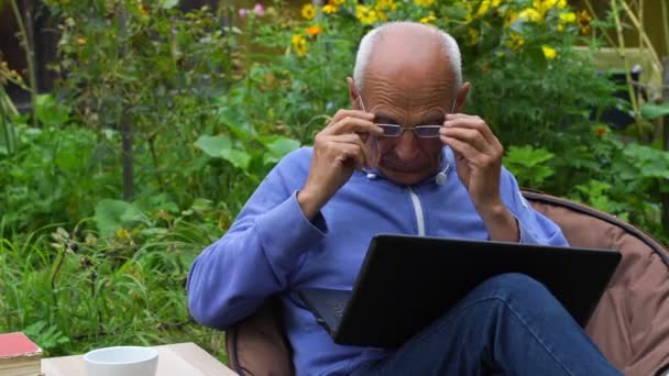 Senior man put on glasses and works on laptop slow motion — Stock video