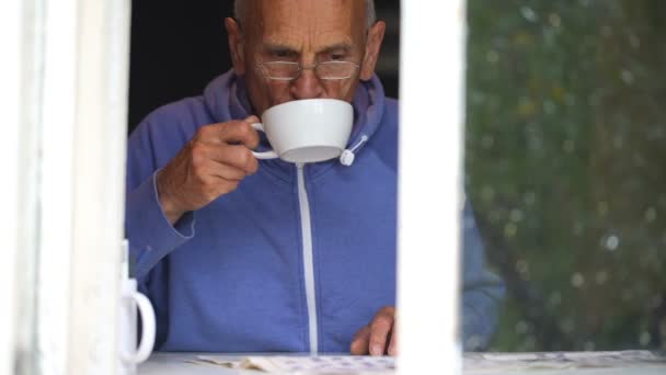 Старик пьет чай и читает на подоконнике замедленной съемки — стоковое видео