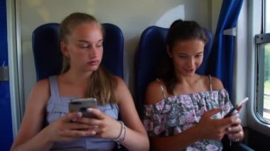 Güzel kızlar trende telefonda sosyal medyayı kullanarak gülerler.