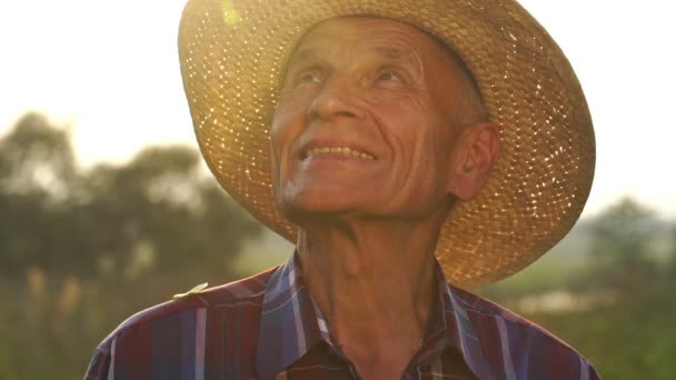 Senior man met strohoed glimlacht naar de zon slow motion — Stockvideo