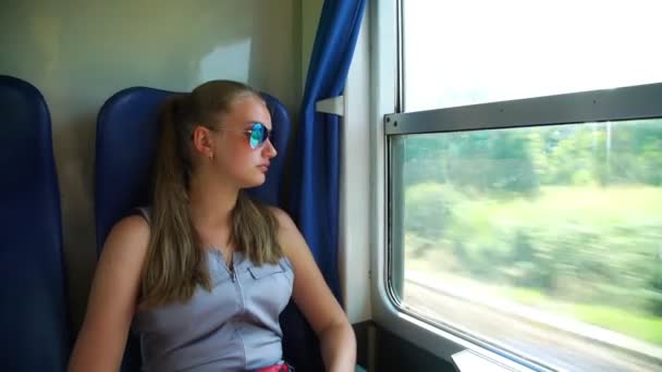 Girl in sunglasses looks out window in train and laughs — Stock Video