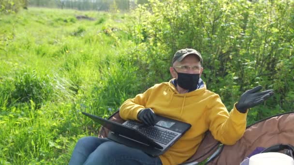 Homem idoso em luvas de máscara fala segurando laptop em joelhos — Vídeo de Stock