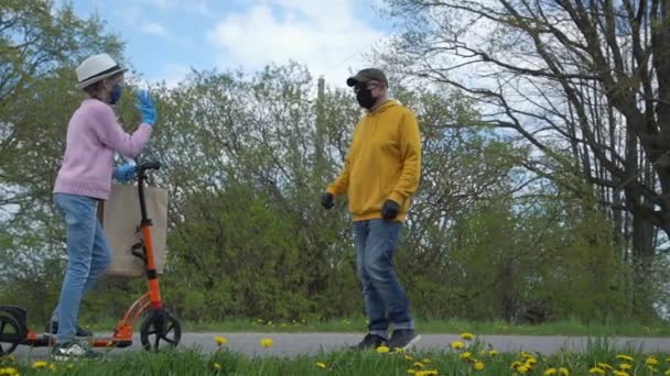 Meisje paardrijden scooter brengt tas naar oude man in masker op de weg — Stockvideo