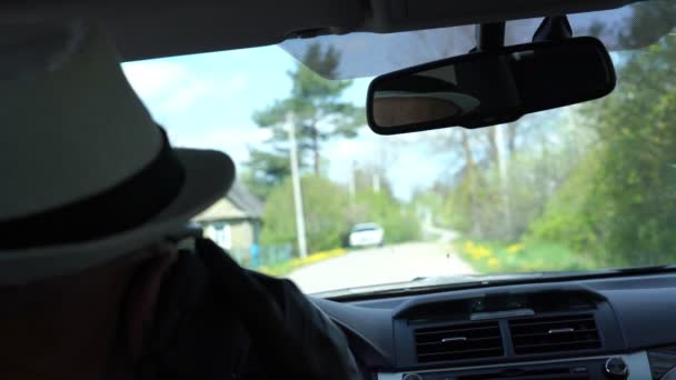 Οδηγός κάθεται στο αυτοκίνητο άποψη από το πίσω κάθισμα και το χωριό έξω — Αρχείο Βίντεο