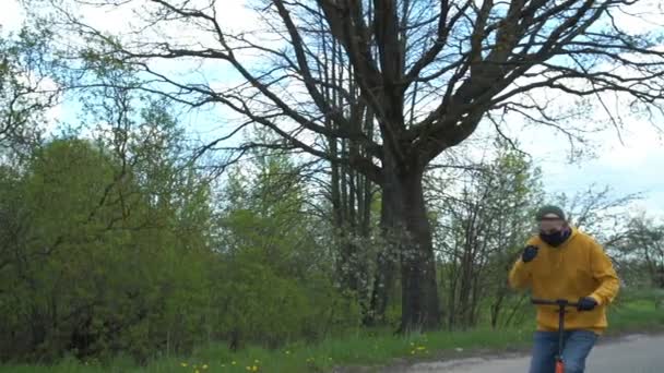 Pensionär i mask handskar rider skoter längs byn väg — Stockvideo