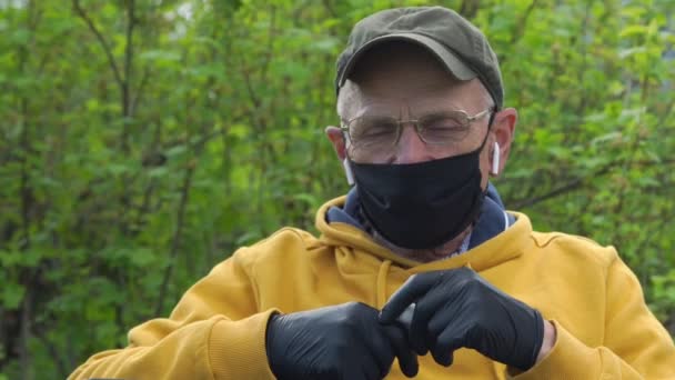 Senior man in masker controleert geluid van draadloze hoofdtelefoon — Stockvideo
