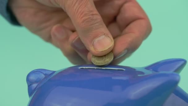 Mão de pessoa velha coloca moedas em ranhura de banco porquinho economizando dinheiro — Vídeo de Stock