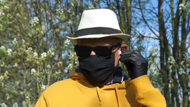 Старик в шляпе и маске надевает наушники и танцы — стоковое видео