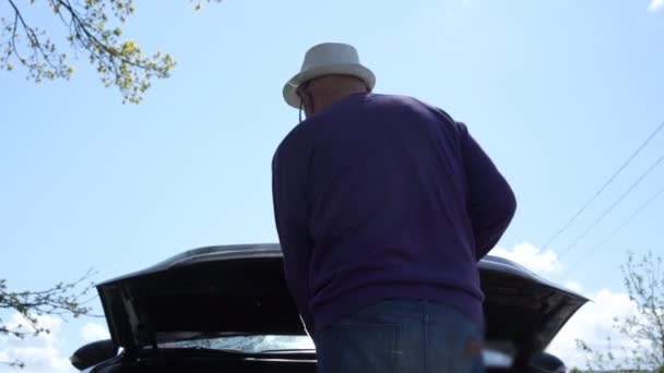 Водитель в фиолетовом свитере поднимает крышку капота смотрит внутрь — стоковое видео