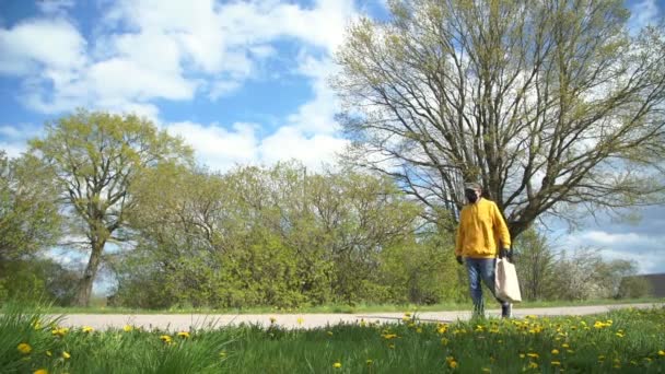 Sarı kapüşonlu yaşlı adam yeşil ağaçların yanından geçiyor. — Stok video