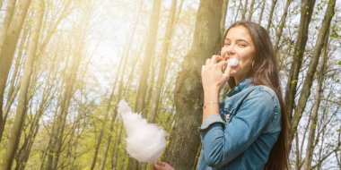 Uzun, dalgalı saçları olan neşeli kadın pamuk helva yiyor.