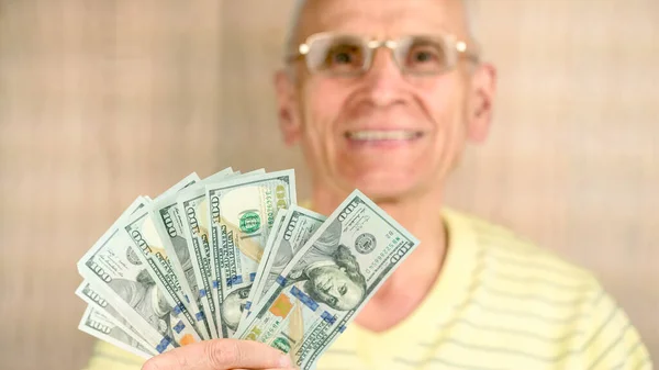 Bulanık gözlüklü yaşlı adam gülümsüyor ve dolarları tutuyor.