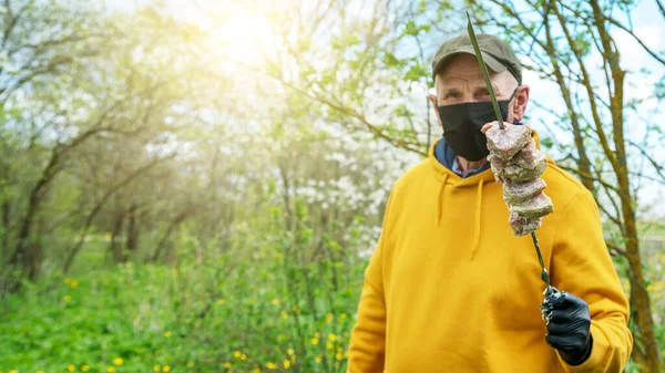 Alter Mann in Maske und Handschuhen hält Spieß mit rohem Fleisch — Stockfoto