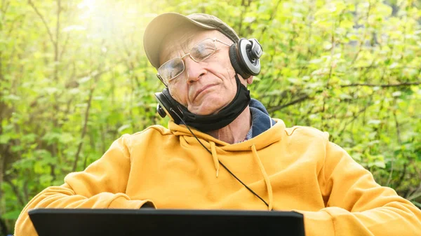 Літній чоловік у навушниках спить на ноутбуці, слухаючи музику — стокове фото