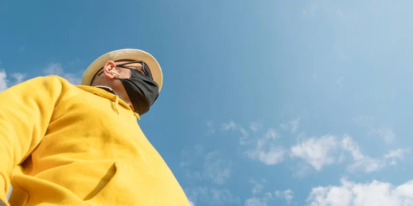 Velho homem de capuz amarelo e máscara preta contra o céu azul — Fotografia de Stock