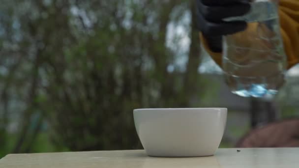 Person in schwarzen Handschuhen gießt Wasser in Tasse auf Gartentisch — Stockvideo