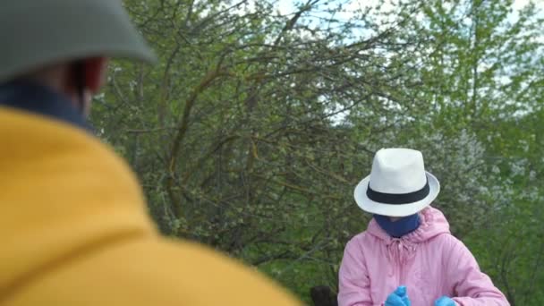 Schoolmeisje in masker spreekt tot opa in geel door bomen — Stockvideo