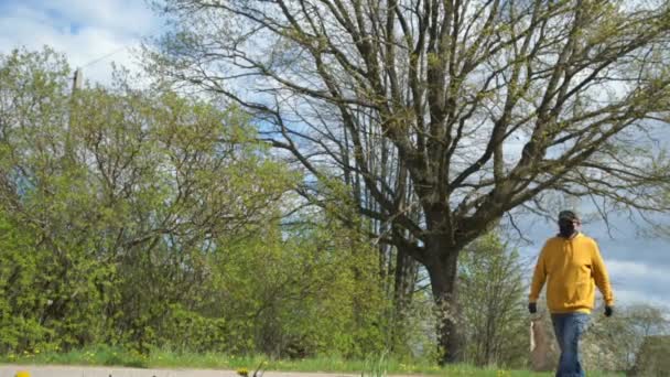 Aged man in black disposable mask and gloves walks past tree — Stock Video