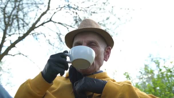 Старий бере чорну одноразову маску і п'є воду — стокове відео
