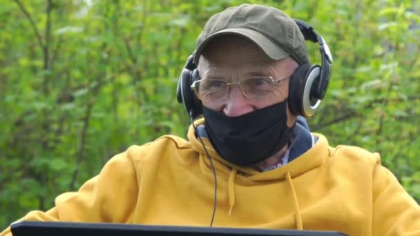 Maskeli emekli internet üzerinden konuşmak için kulaklık kullanıyor — Stok video