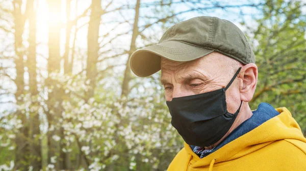 Pensioner em boné e preto máscara fica no jardim closeup — Fotografia de Stock