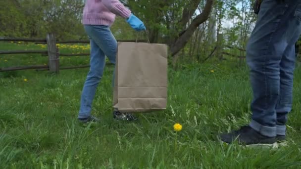 Chica en jeans trae bolsa de papel con productos a anciano — Vídeos de Stock