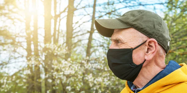 Homem sênior em boné e preto máscara fica no jardim closeup — Fotografia de Stock