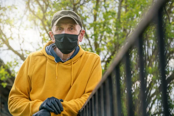 Старший человек в черной маске опирается на забор в загородном доме — стоковое фото