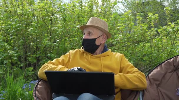 Pensionato in felpa gialla con cappuccio e maschera nera funziona su laptop — Video Stock