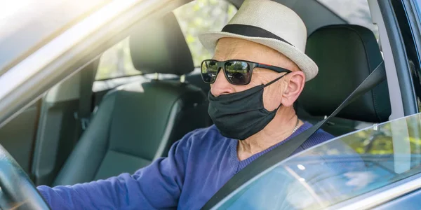 Beyaz şapkalı ve siyah maskeli emekli sürücü arabada oturuyor.