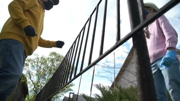 Skolflicka pratar med farfar i mask med staket på avstånd — Stockvideo