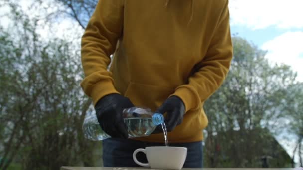 Person in schwarzen Handschuhen gießt Wasser in Tasse und Getränke — Stockvideo