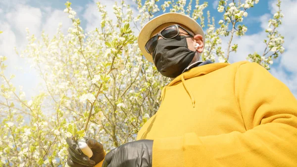 pensioner in facial mask against garden tree in blossom