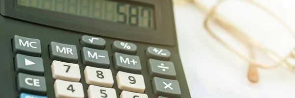 black vintage calculator on table against blurry glasses