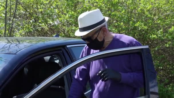 Oude man in zwart wegwerp masker handschoenen krijgt in auto — Stockvideo